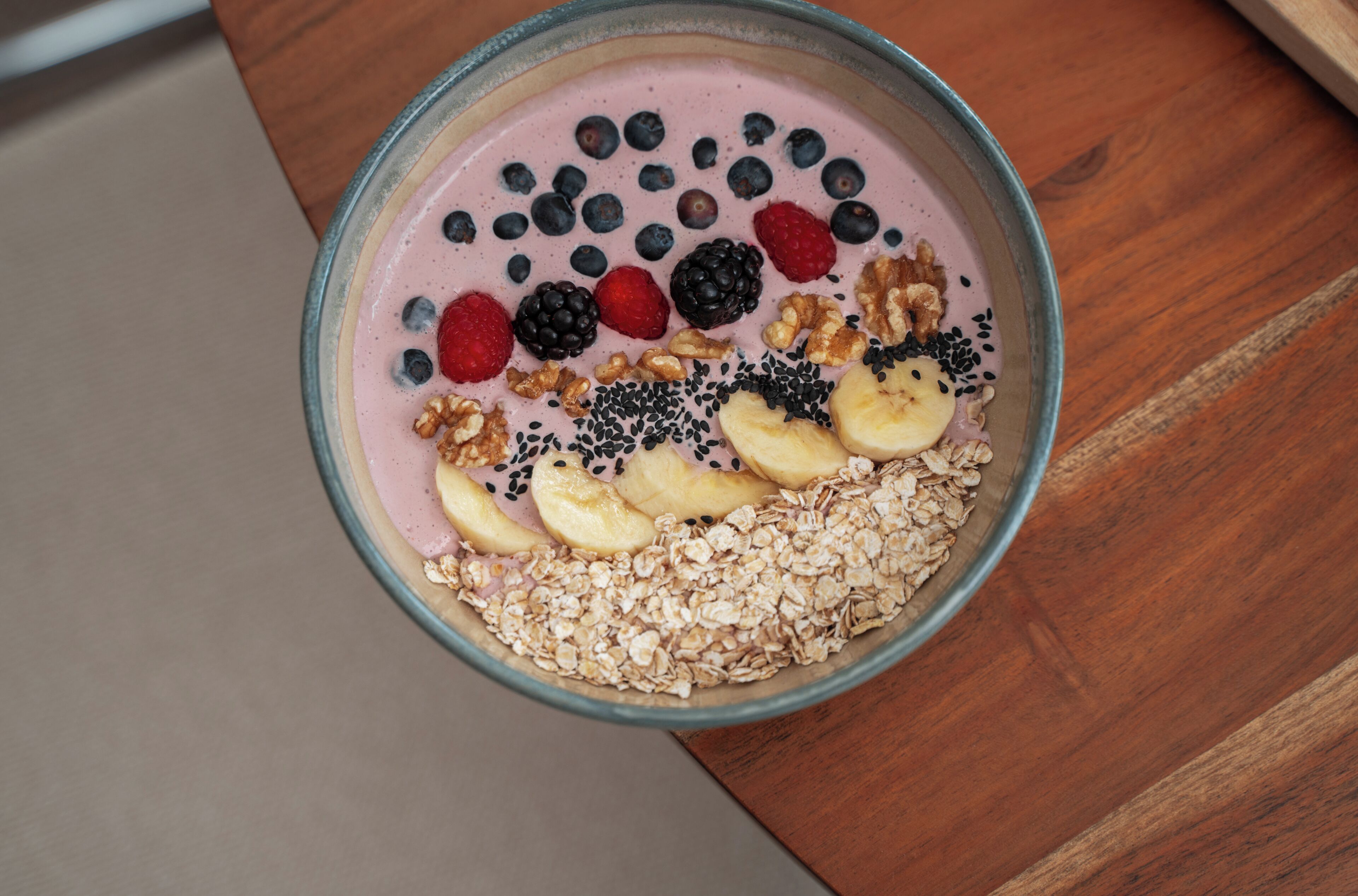 En skål med smoothie, frukt och granola på ett träbord.