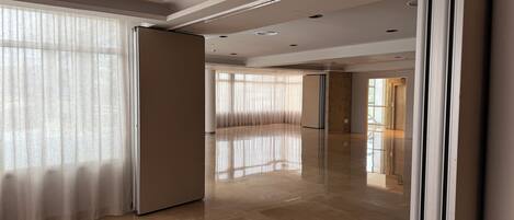 A spacious, modern hotel lobby with a polished marble floor, large windows with sheer curtains, and a sleek, contemporary design.