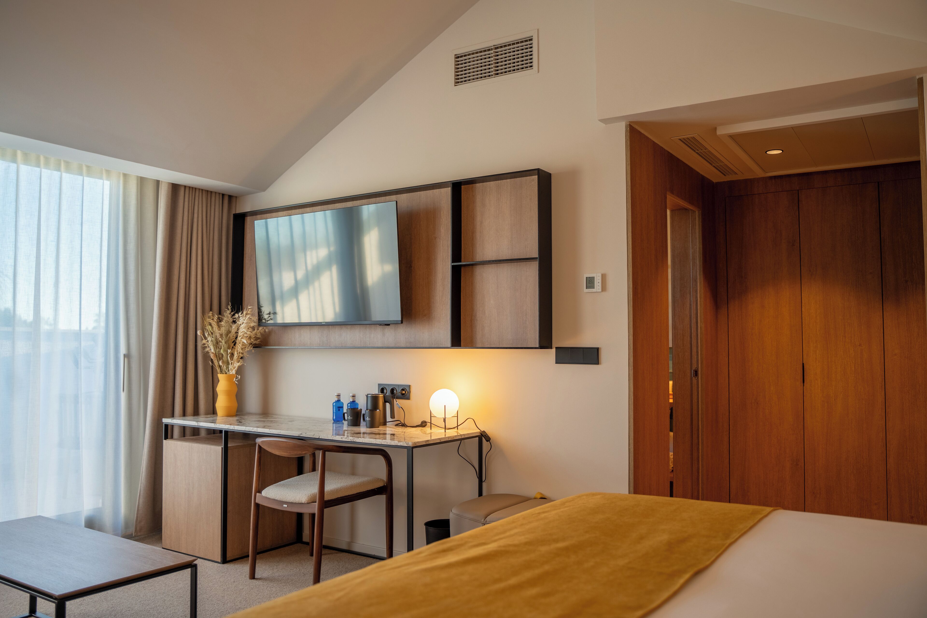 Ein Hotelzimmer mit einem Bett, einem Schreibtisch mit Stuhl, einem an der Wand befestigten Fernseher und einem Kleiderschrank.
