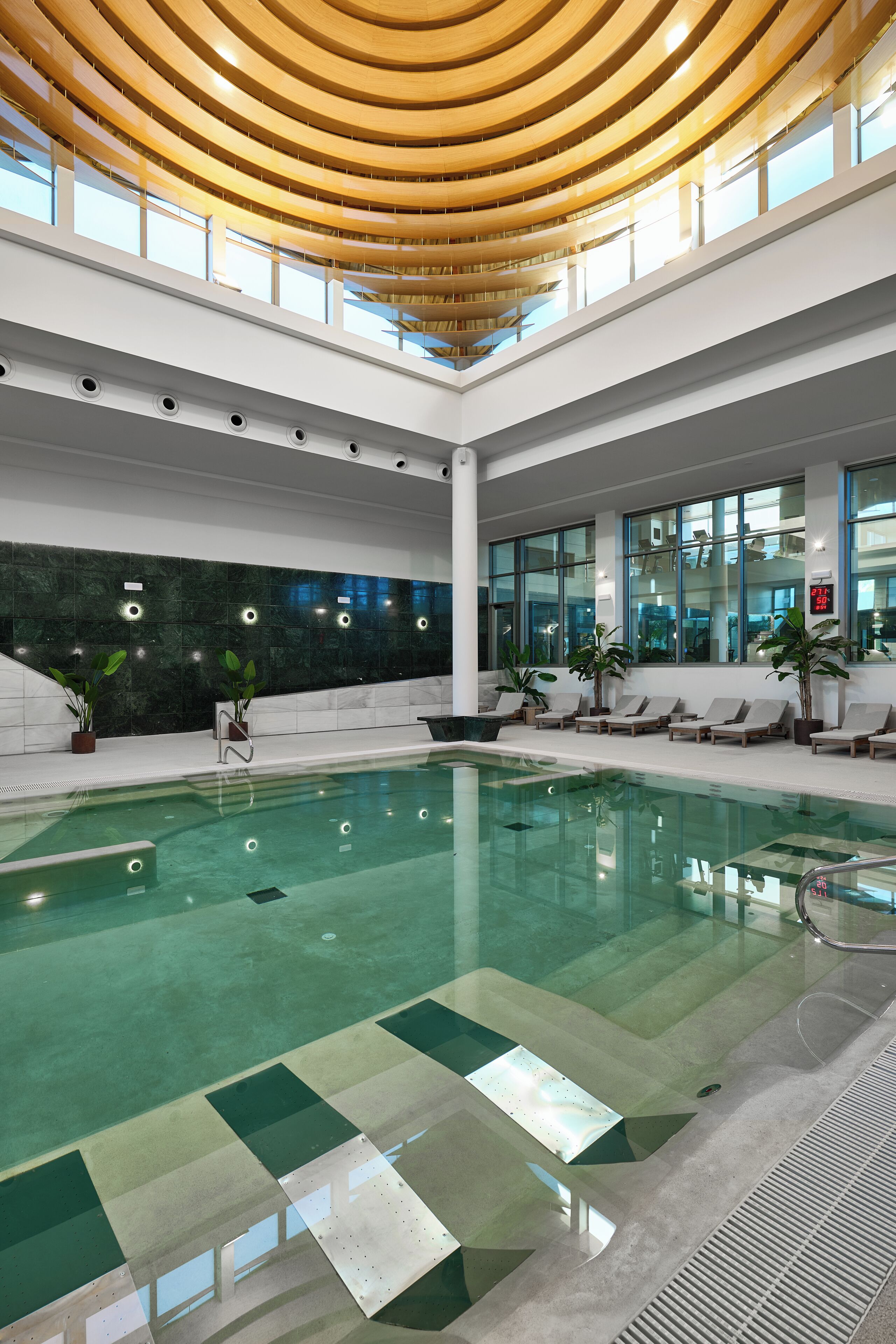 Una piscina interior de diseño moderno, rodeada de zonas de descanso y amplias ventanas.