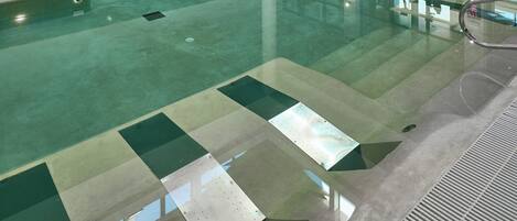 Una piscina interior de diseño moderno, rodeada de zonas de descanso y amplias ventanas.