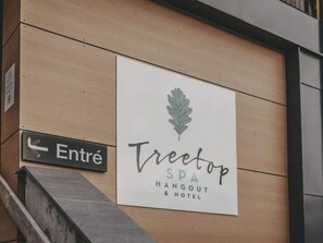 Placa com o nome 'Treetop SPA HANGOUT & HOTEL', um logotipo de folha e uma placa 'Entré' indicando a entrada.