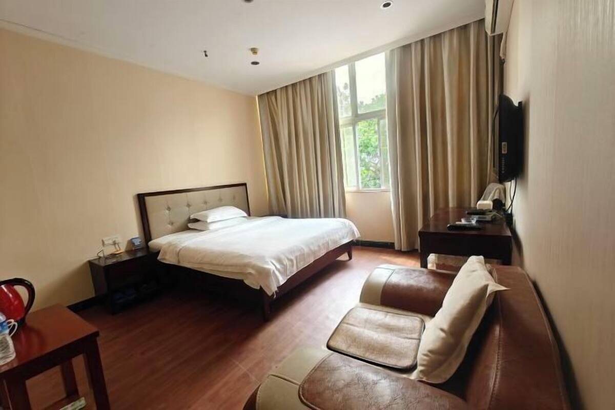 A hotel room with a bed, a sofa, a TV, and a window with curtains.