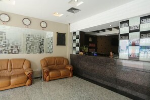 A reception area with two leather sofas, a reception desk, and a wall with patterned decorations. - Haidian Resort Hotel (Beihai)