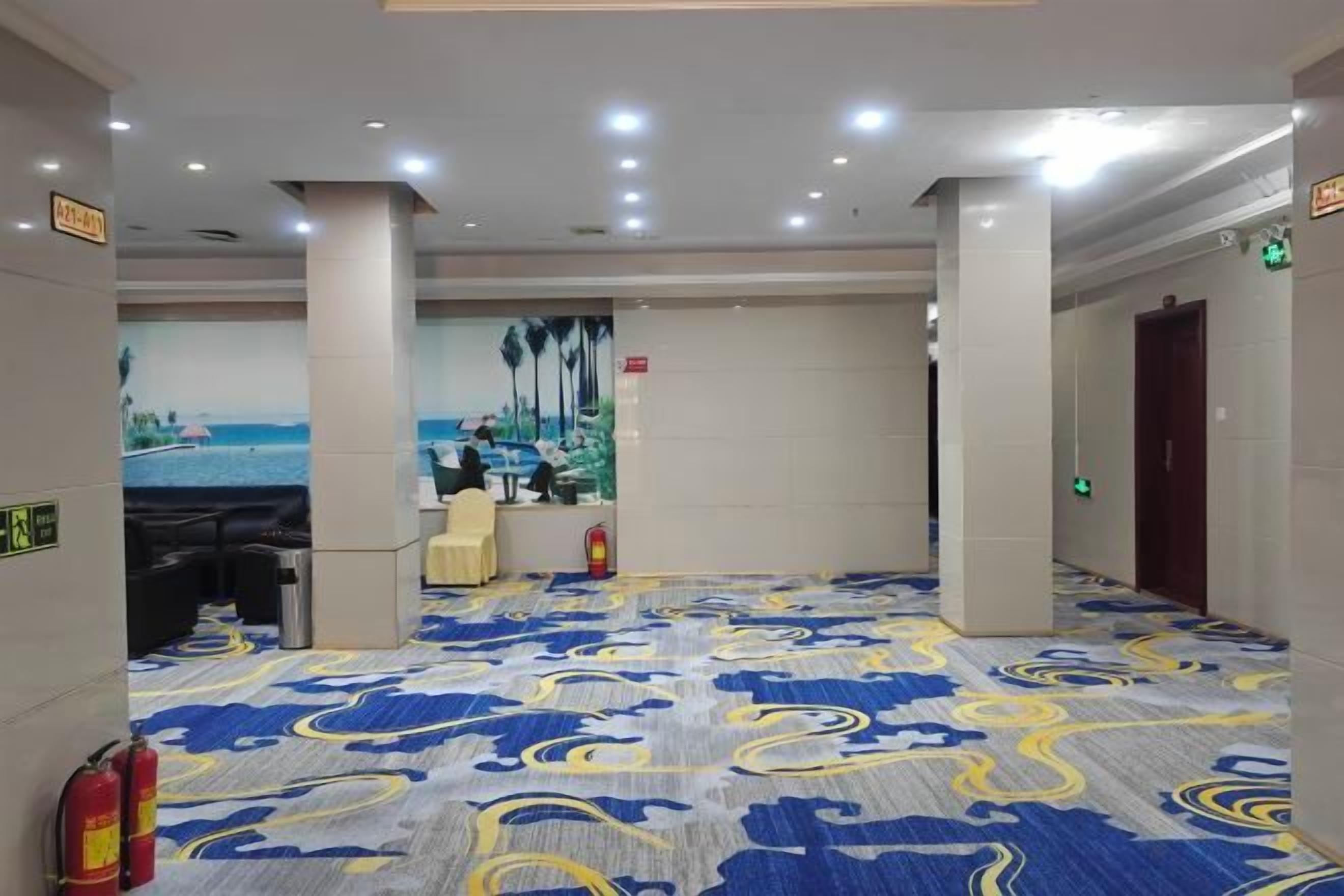 A hotel lobby with a patterned carpet, a reception desk, and a mural of a beach scene.
