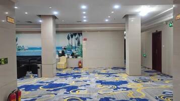 A hotel lobby with a patterned carpet, a reception desk, and a mural of a beach scene.