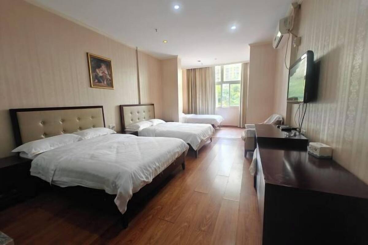 A hotel room with three beds, a desk, a TV, and a window.