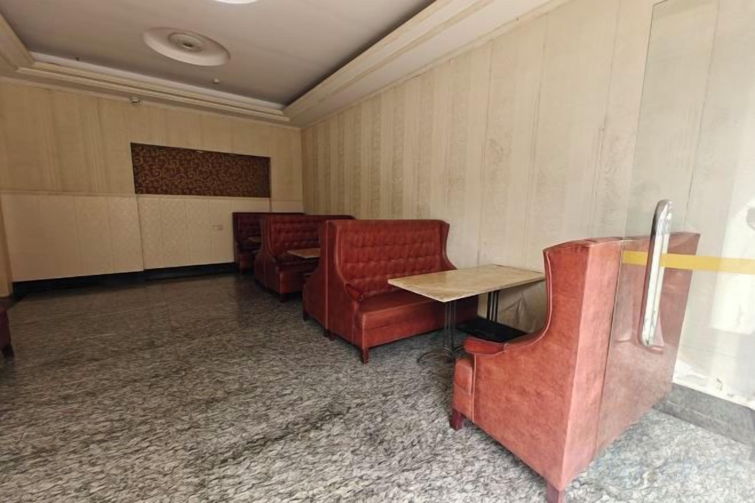 A room with a carpeted floor, a wooden panel wall, and a red upholstered booth.