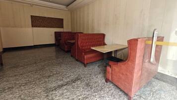 A room with a carpeted floor, a wooden panel wall, and a red upholstered booth.