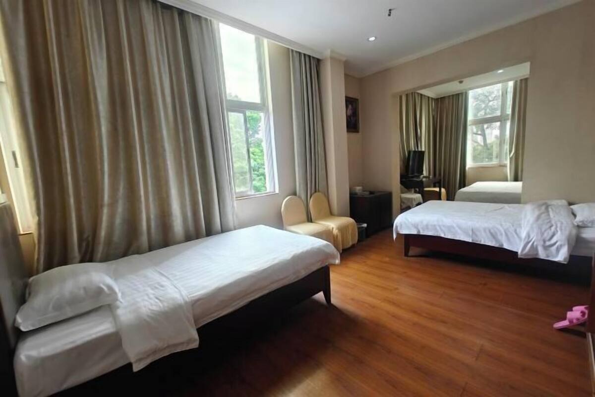 A hotel room with two single beds, a wooden floor, a TV, and a large window with curtains.