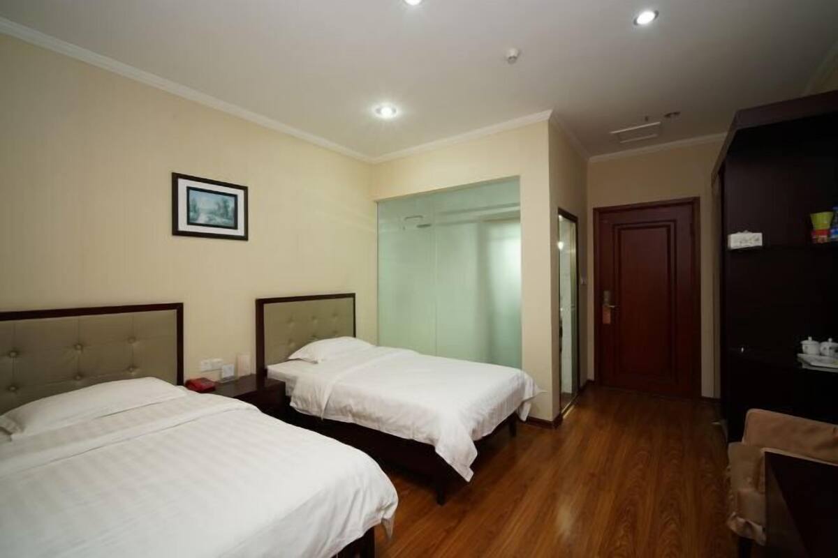 A hotel room with two beds, a wooden floor, a door, and a framed picture on the wall.