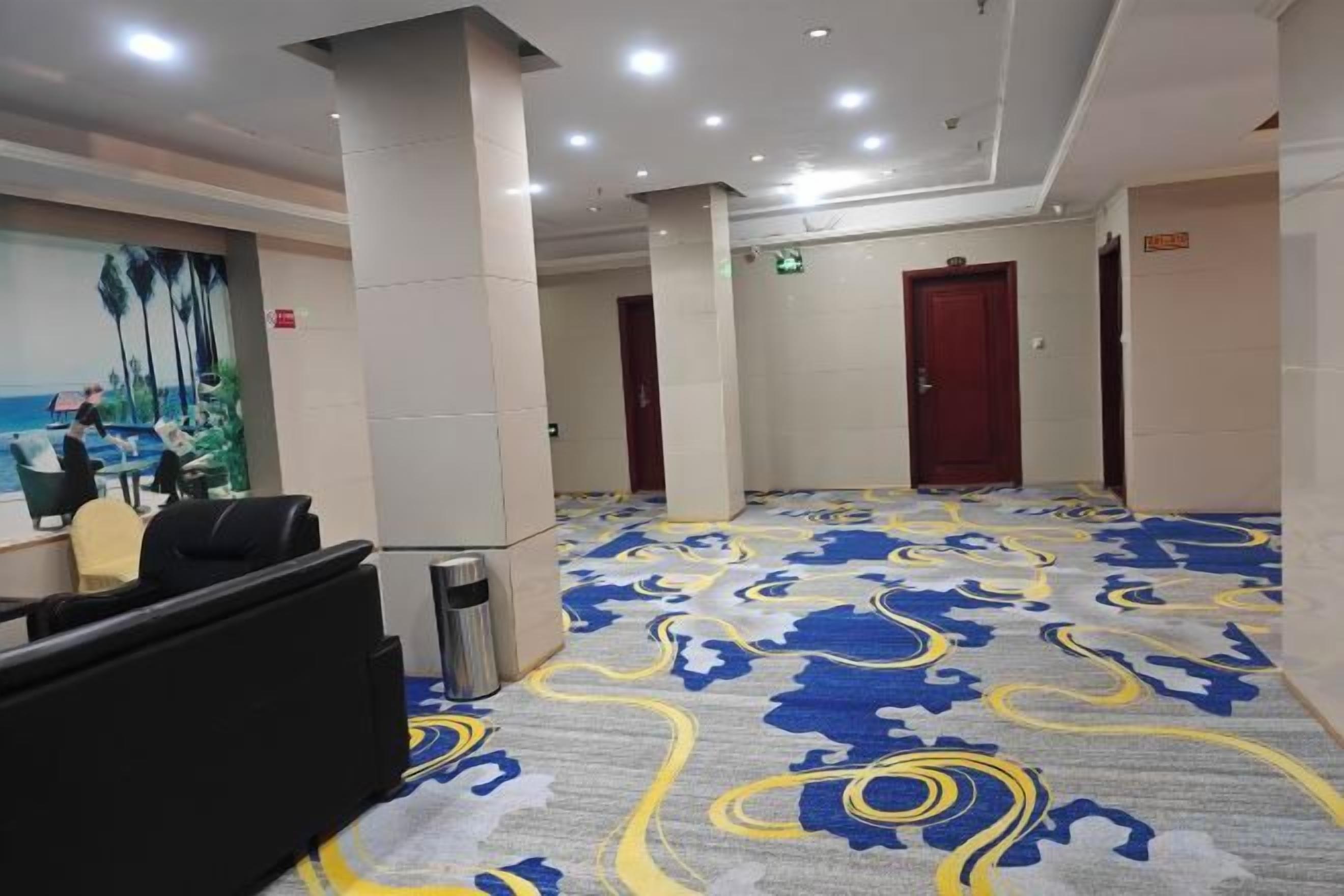 A hotel lobby with a patterned carpet, a reception desk, and a painting on the wall.