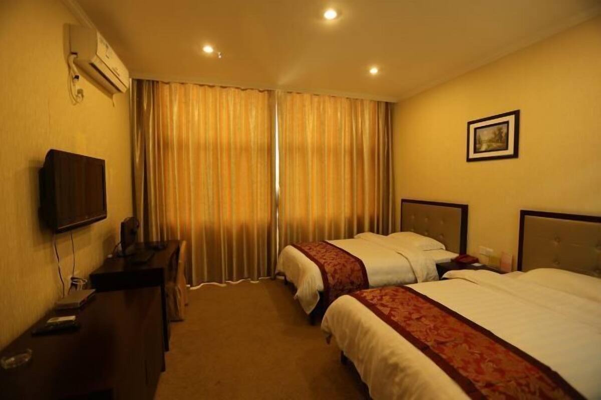 A hotel room with two beds, a desk, a television, and curtains.