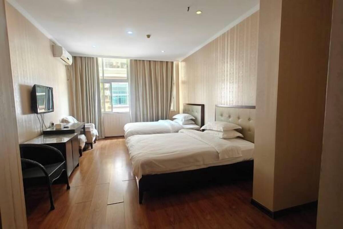 A hotel room with two beds, a desk, a chair, a TV, and a window with curtains.