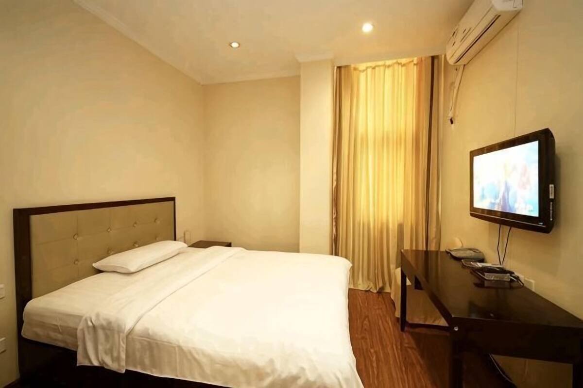 A hotel room with a bed, a desk with a television, and a window with curtains.
