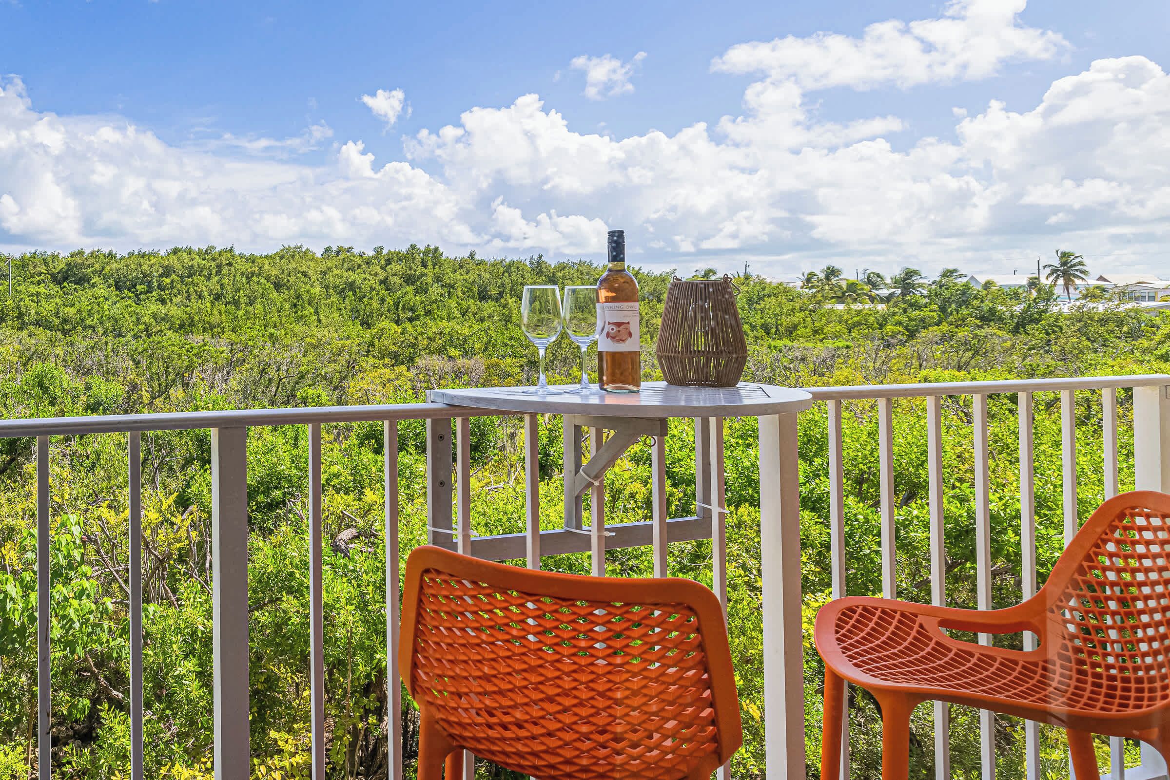 A balcony with a table, two chairs, a bottle of wine, and glasses.