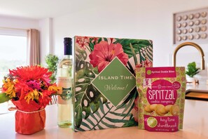 A kitchen counter with a bottle of Winking's, a box of Spritzal cookie bites, and a vase of flowers. - Island Time | 2 King Suites | Ocean Pointe 1203 (Tavernier)