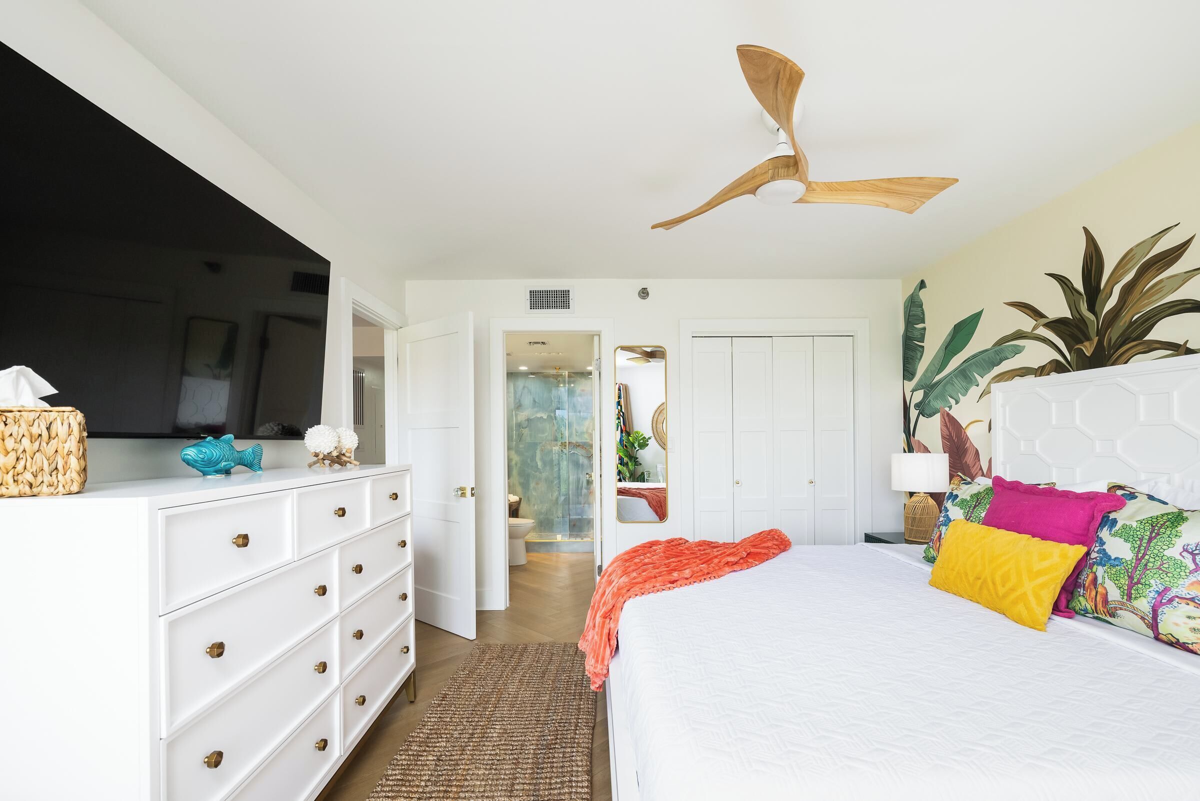 A bedroom with a bed, white dresser, ceiling fan, and a TV on the dresser.
