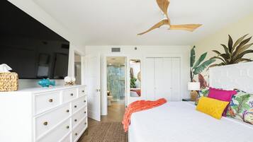 A bedroom with a bed, white dresser, ceiling fan, and a TV on the dresser.