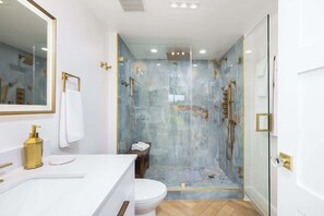 A modern bathroom with a glass-enclosed shower, a white sink with gold fixtures, and a wooden bench.
