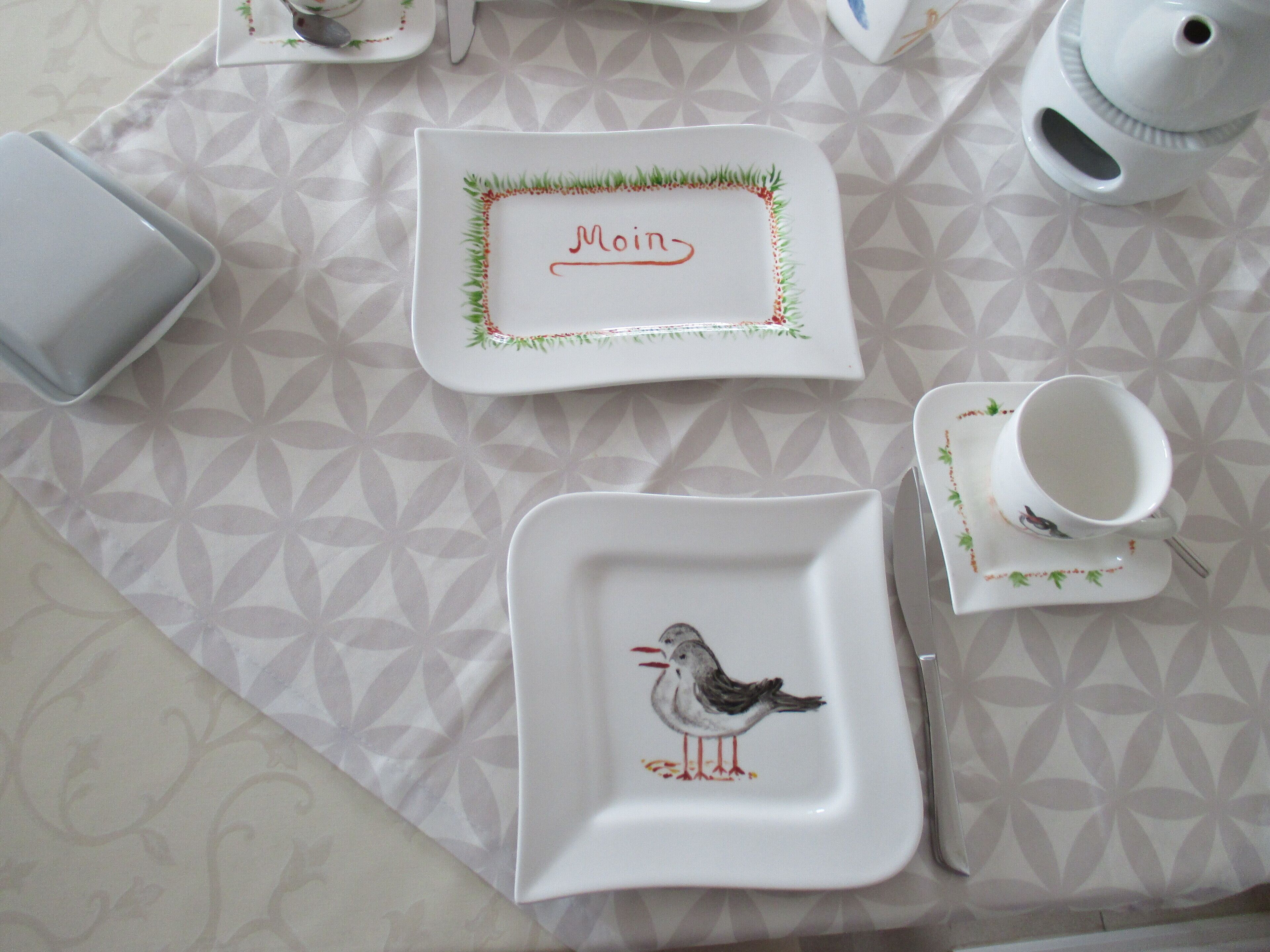 A table set with white plates, a cup, and a teapot on a patterned tablecloth.