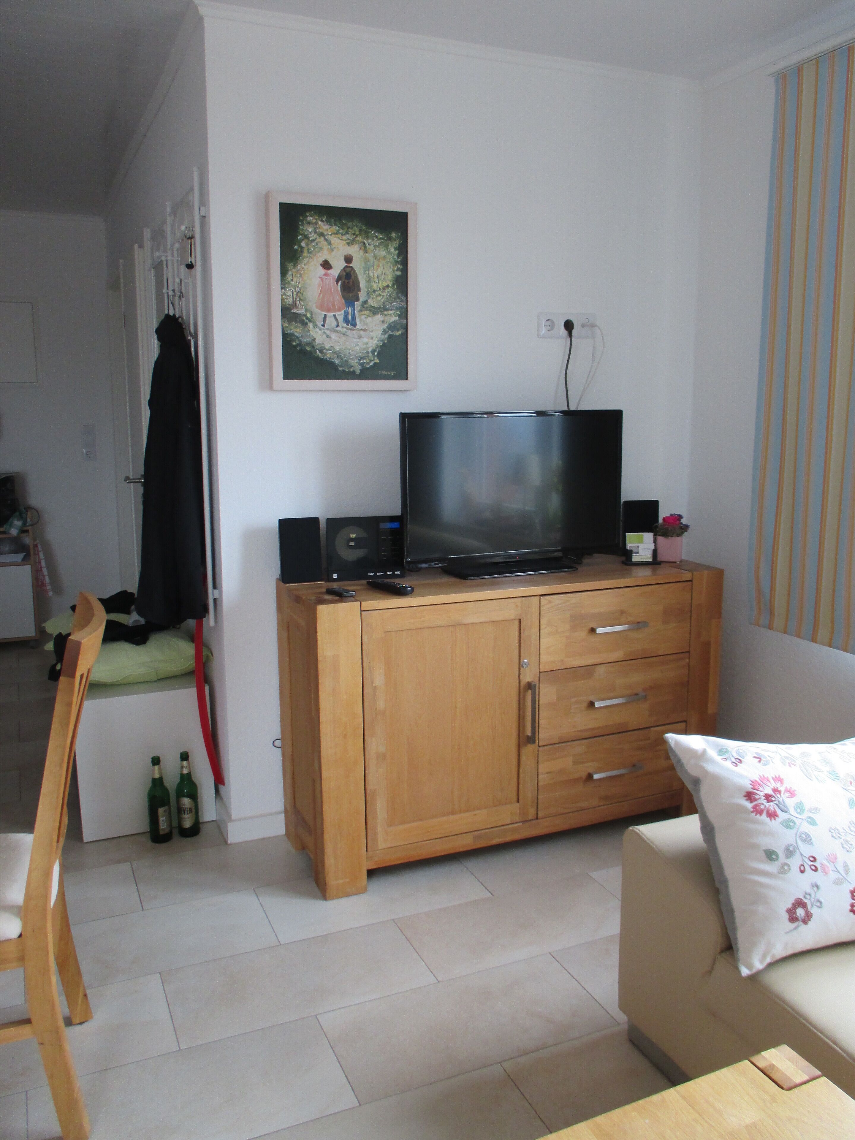 A living room with a wooden cabinet, a television, and a painting on the wall.