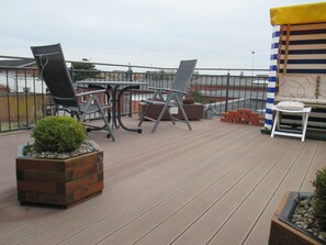Eine Terrass mit Tisch und Stühlen, Blumentöpfen und einem gestreiften Sonnendach.
