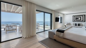 A modern hotel room with a large bed, a TV, and a view of the ocean.
