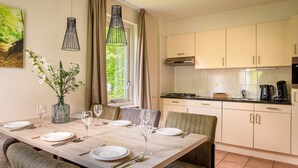 Una cocina moderna con armarios blancos, una mesa de comedor para cuatro personas y vistas a zonas verdes.