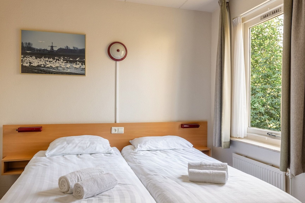 Habitación de hotel con dos camas, un reloj, un cuadro en la pared y una ventana con cortinas.