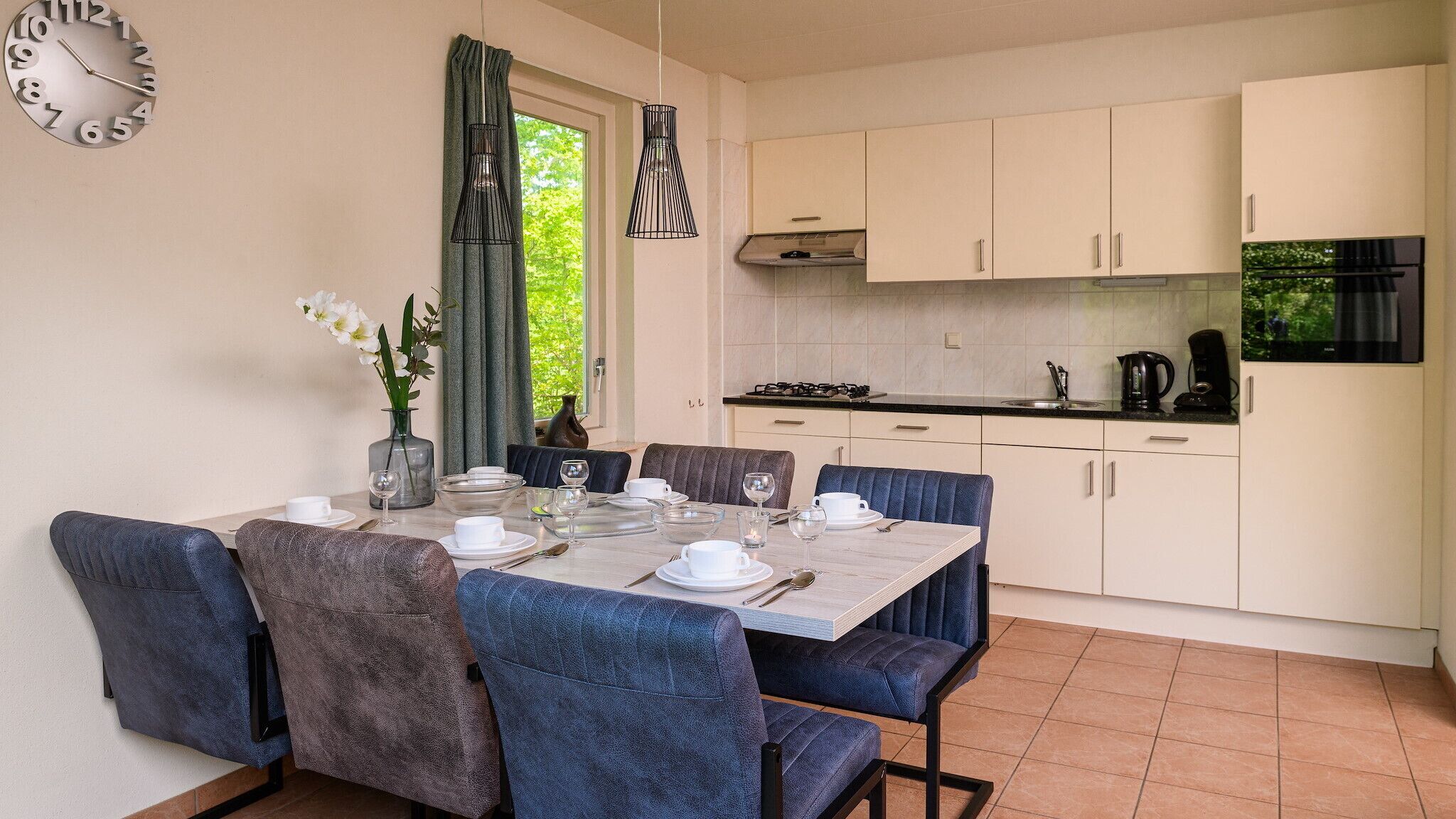 A modern kitchen with white cabinets, a dining table set for four, and a clock on the wall.