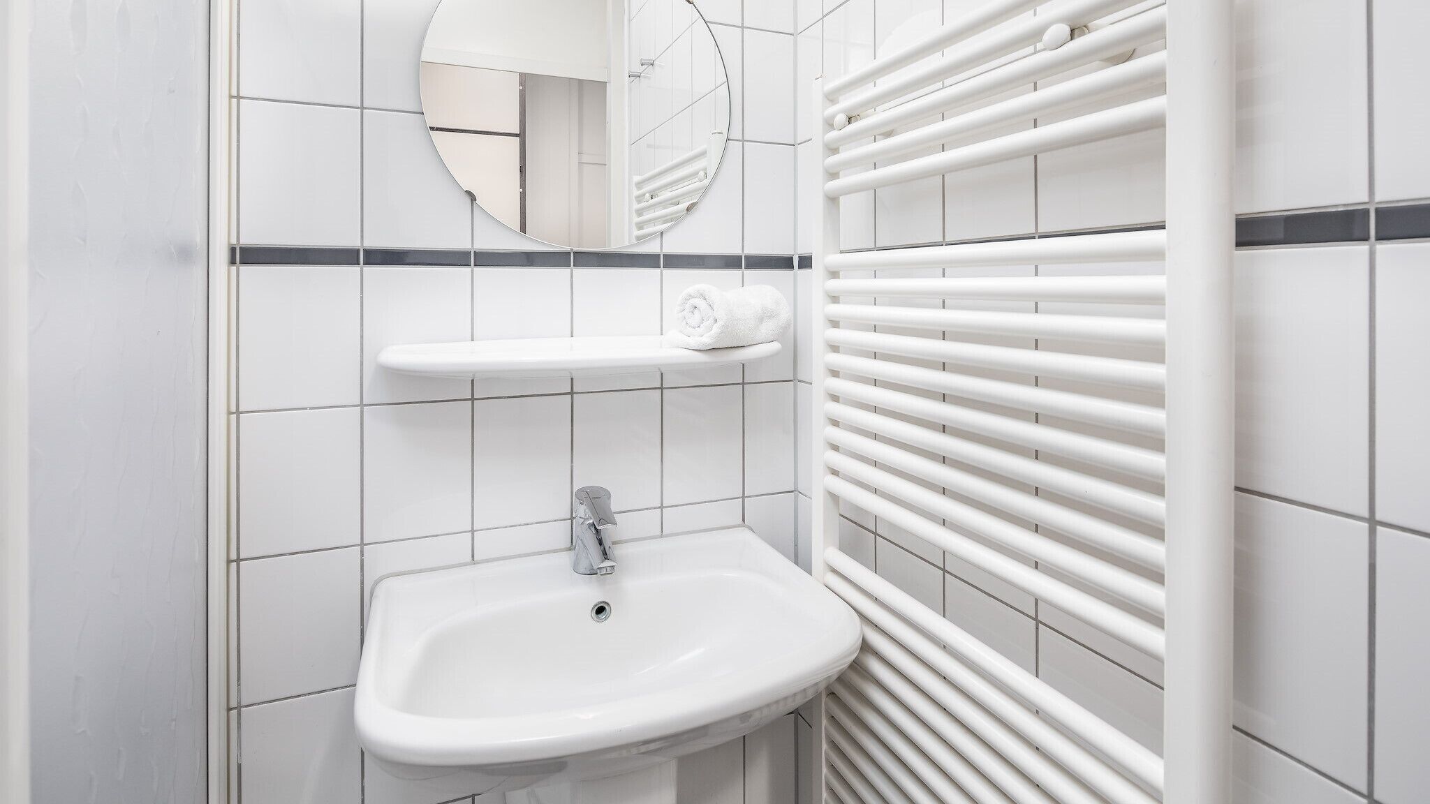 Een moderne badkamer met een wit wastafel, een spiegel en een handdoekhouder.