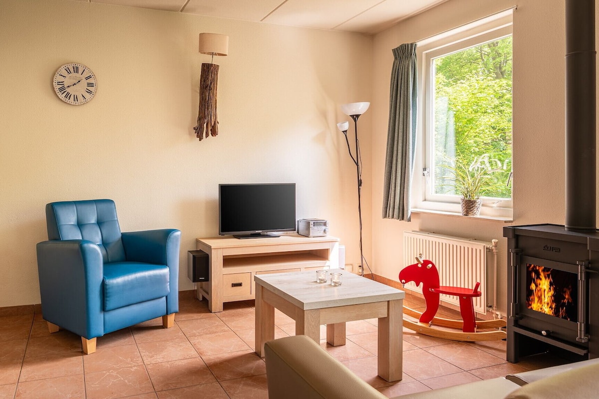 Una sala de estar con un sillón azul, televisor, una mesita, un reloj y una chimenea.