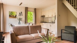 Una sala moderna con un sofá color beige, una mesa de comedor y una zona de cocina con armarios blancos y encimera negra.