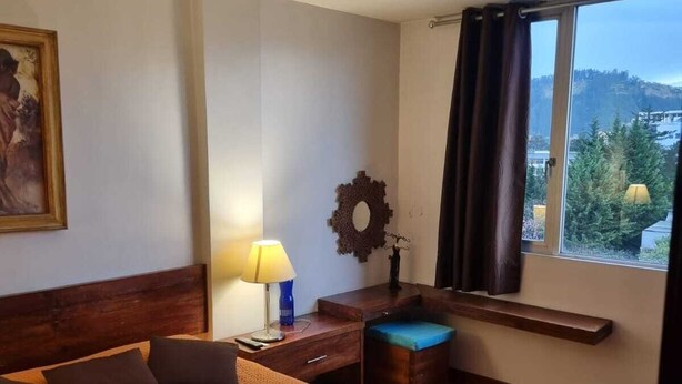A hotel room with a large bed, a desk, a chair, a window with a view, and a painting on the wall. - Lovely Suite w/good internet perfect for digital nomads (Quito)