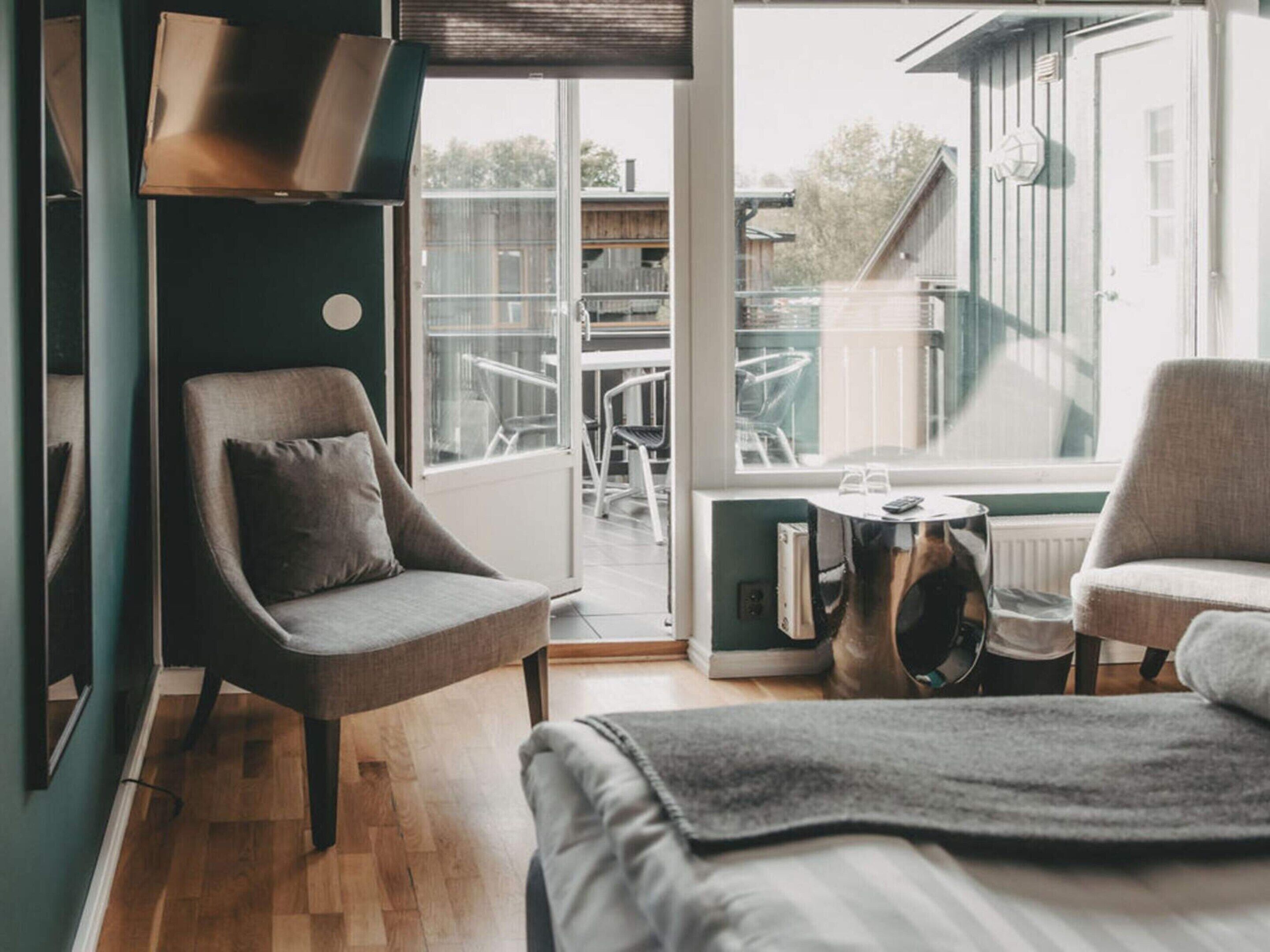 Ett modernt hotellrum med en säng, två fåtöljer, ett litet bord och ett stort fönster med utsikt över utomhusområdet.