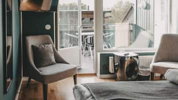 Ett modernt hotellrum med en säng, två fåtöljer, ett litet bord och ett stort fönster med utsikt över utomhusområdet.