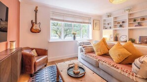 Una sala de estar acogedora con un sofá de cuero, una mesa de centro con una vela, una guitarra en la pared y una estantería con objetos decorativos.