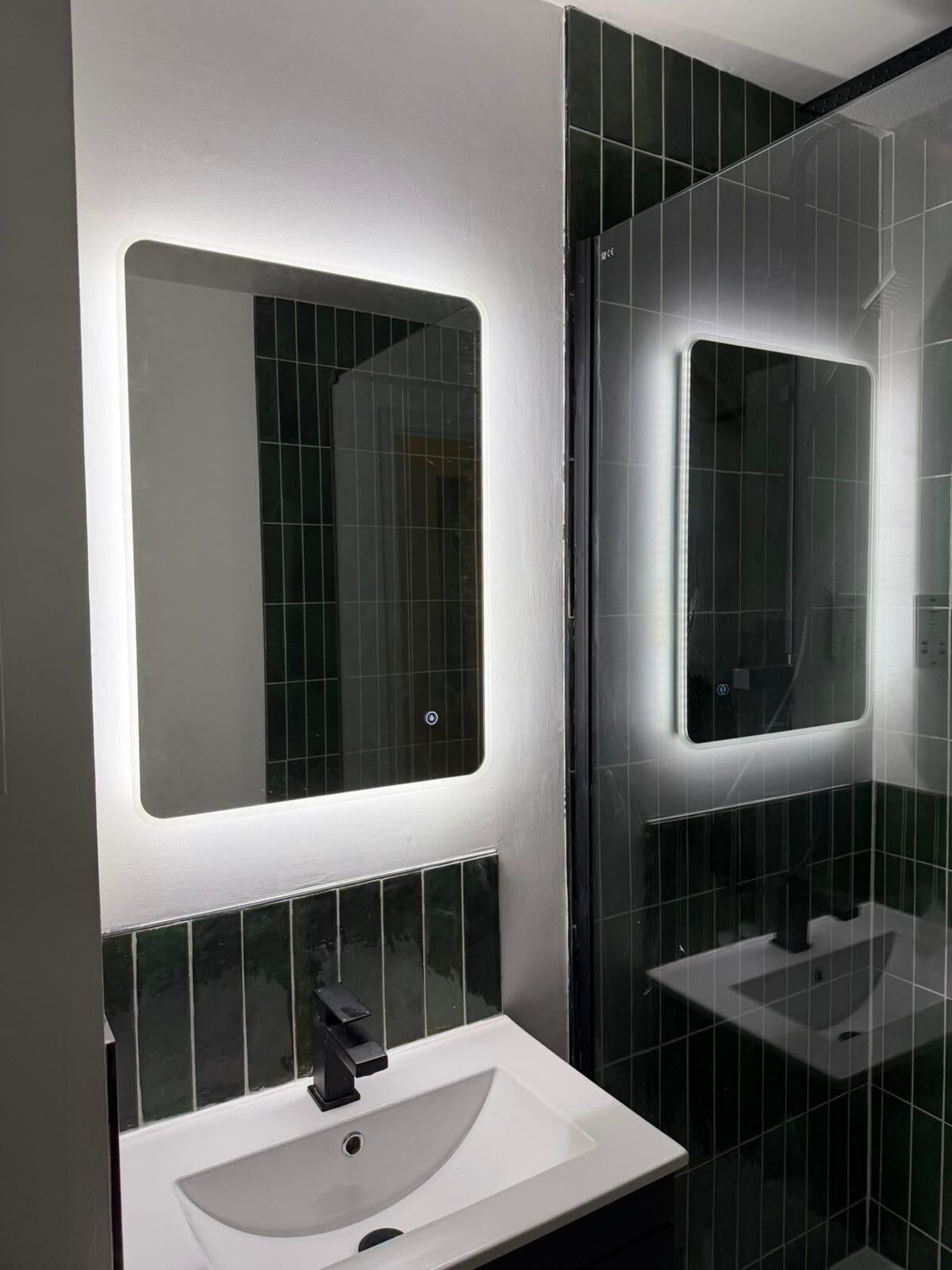 Un bagno moderno con un lavandino bianco, uno specchio e pareti rivestite di piastrelle nere.