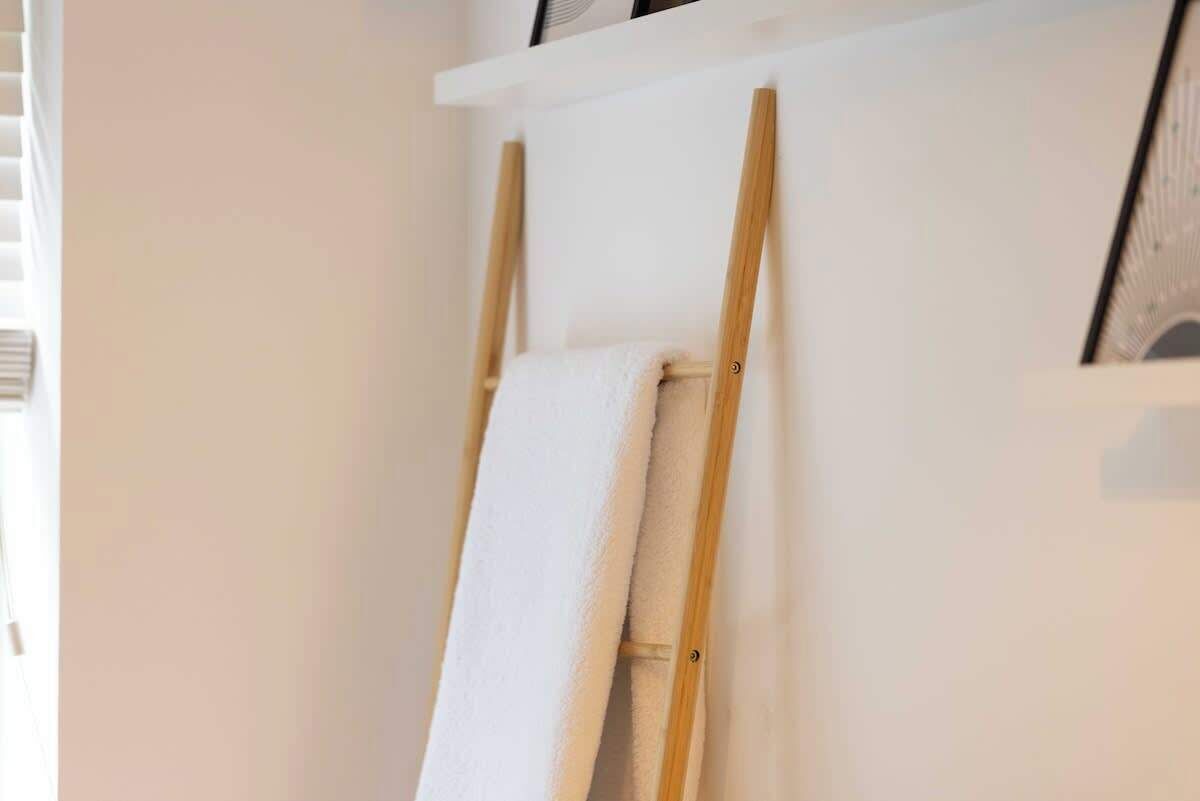 Eine weiße Wand mit einer hölzernen Staffelei, auf der ein aufgerolltes weißes Handtuch liegt.