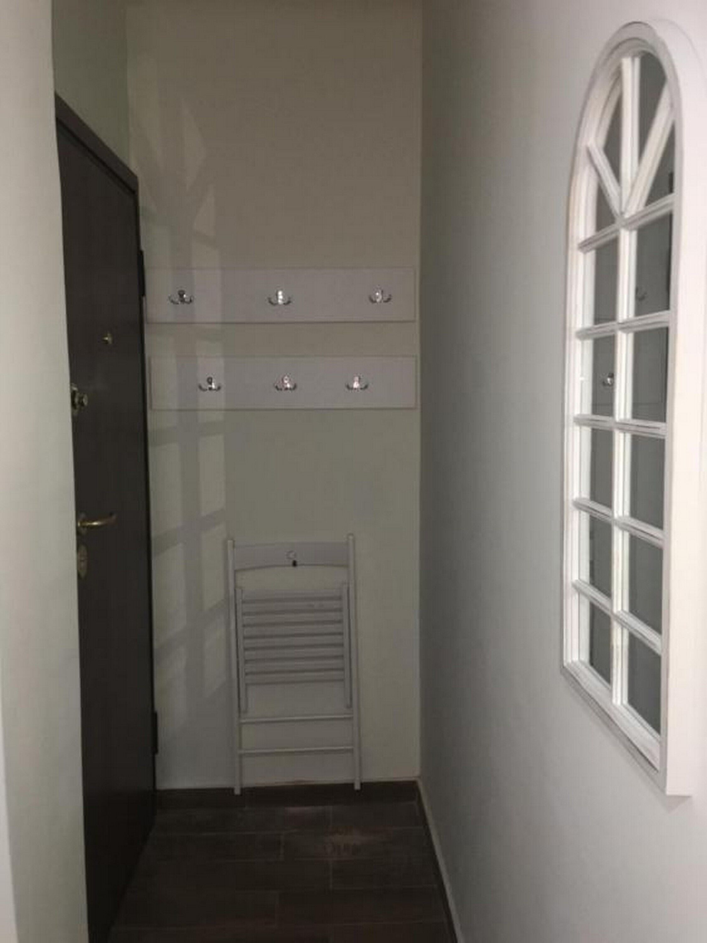 Un couloir étroit avec une porte sombre, un mur blanc et une fenêtre blanche.