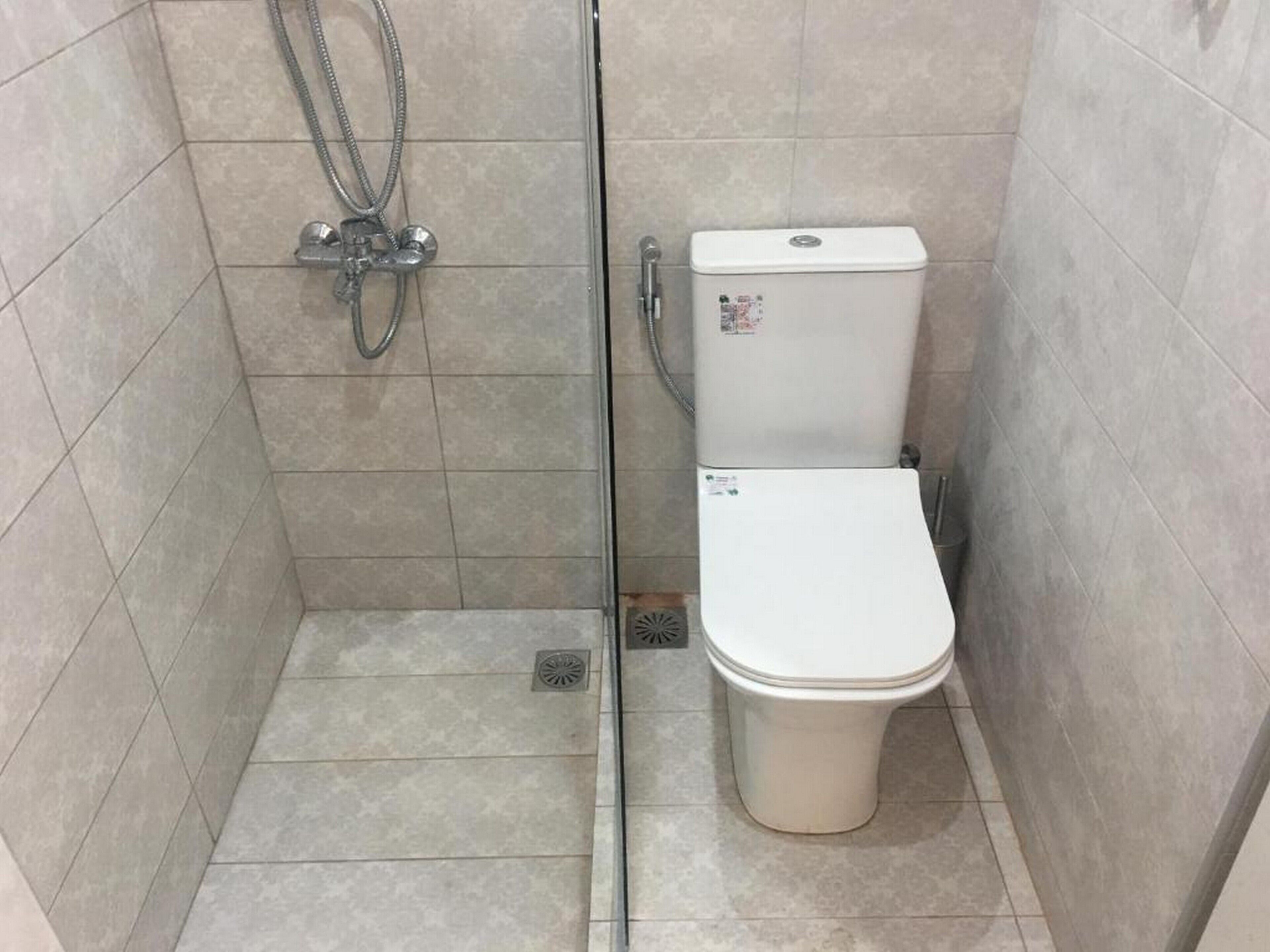 A small, tiled bathroom with a toilet and a shower.