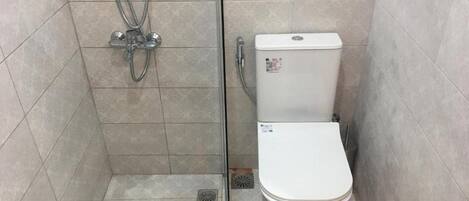 A small, tiled bathroom with a toilet and a shower.