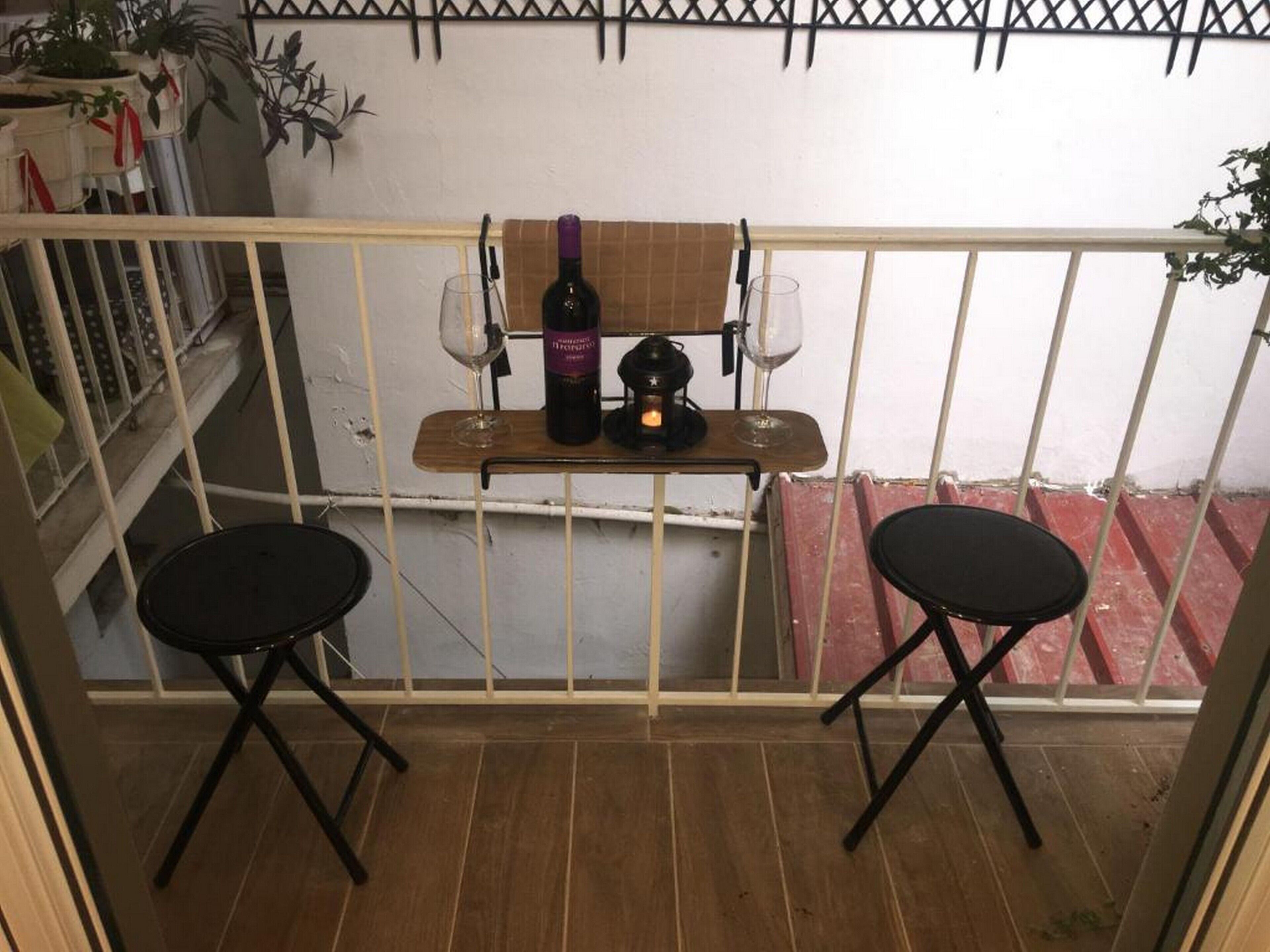 A balcony with two black chairs, a small table with a bottle of wine, two wine glasses, and a candle.