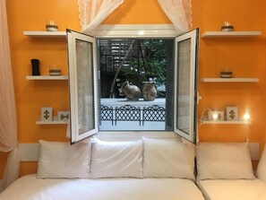 A bedroom with a bed, white bedding, and a window with a view of outdoor pots and a fence. - Amalthea Studio (Athens)