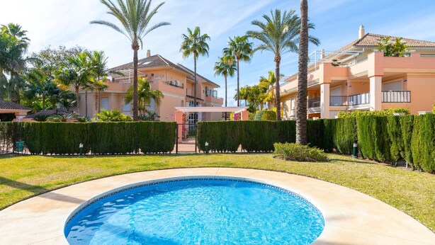 A swimming pool surrounded by a well-maintained lawn and palm trees, with a building in the background. - Mar Bella in Marbella (Marbella)