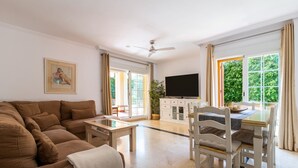 A living room with a brown sectional sofa, a wooden coffee table, a dining table with white chairs, a flat-screen TV, and a ceiling fan. - Mar Bella in Marbella (Marbella)