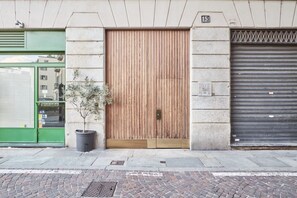 A building facade with a large wooden door, a green storefront, and a closed metal shutter.