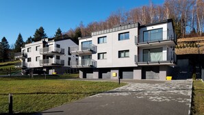A modern multi-story residential building with balconies, a paved driveway, and a grassy area in front. - Apartamenty Sun & Snow Poniwiec (Ustron)