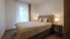A bedroom with a bed, two bedside lamps, a window with curtains, and a wooden floor. - Apartamenty Sun & Snow Poniwiec (Ustron)